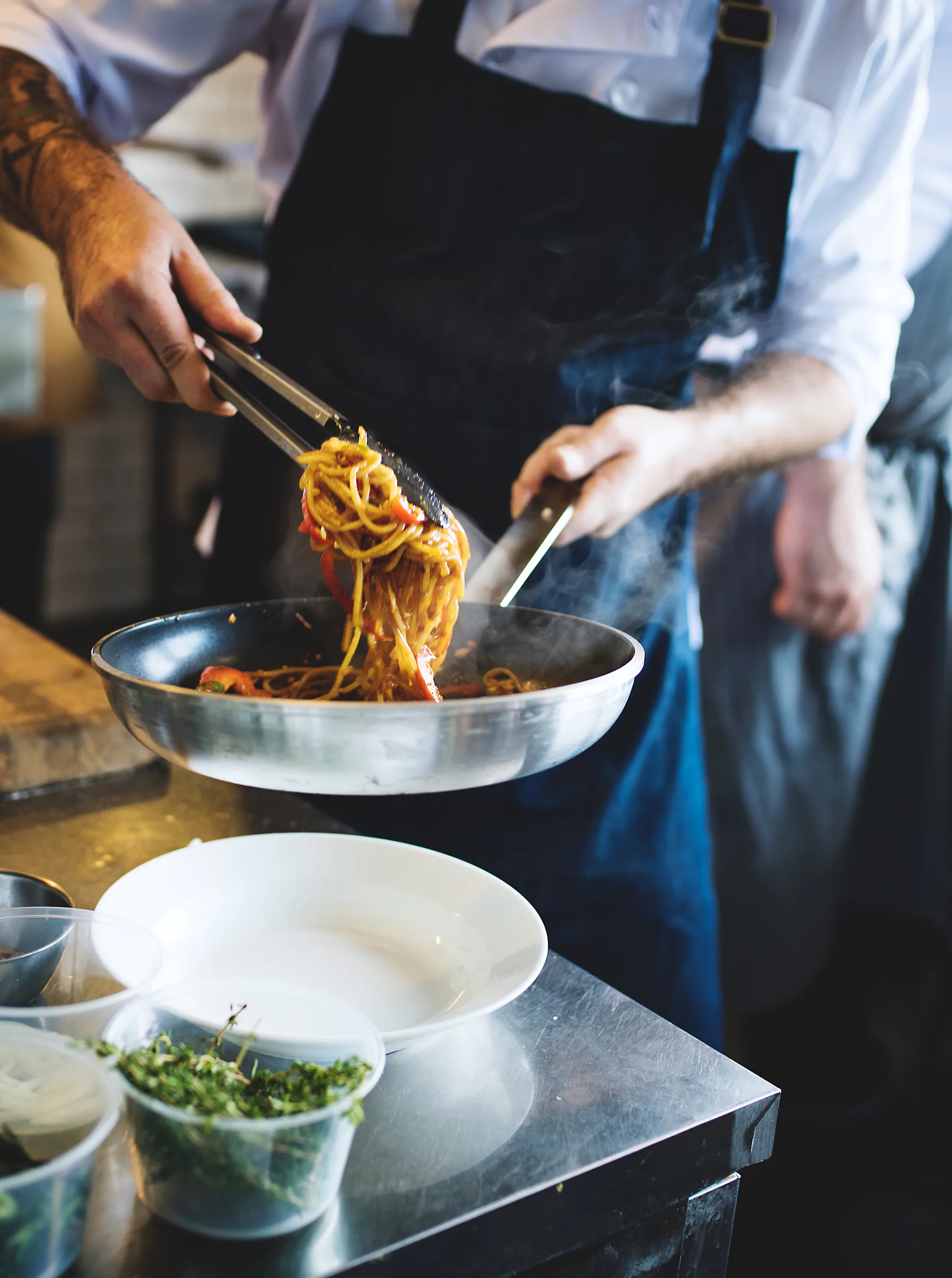 Chef preparando pasta en una sartén dentro de una cocina profesional