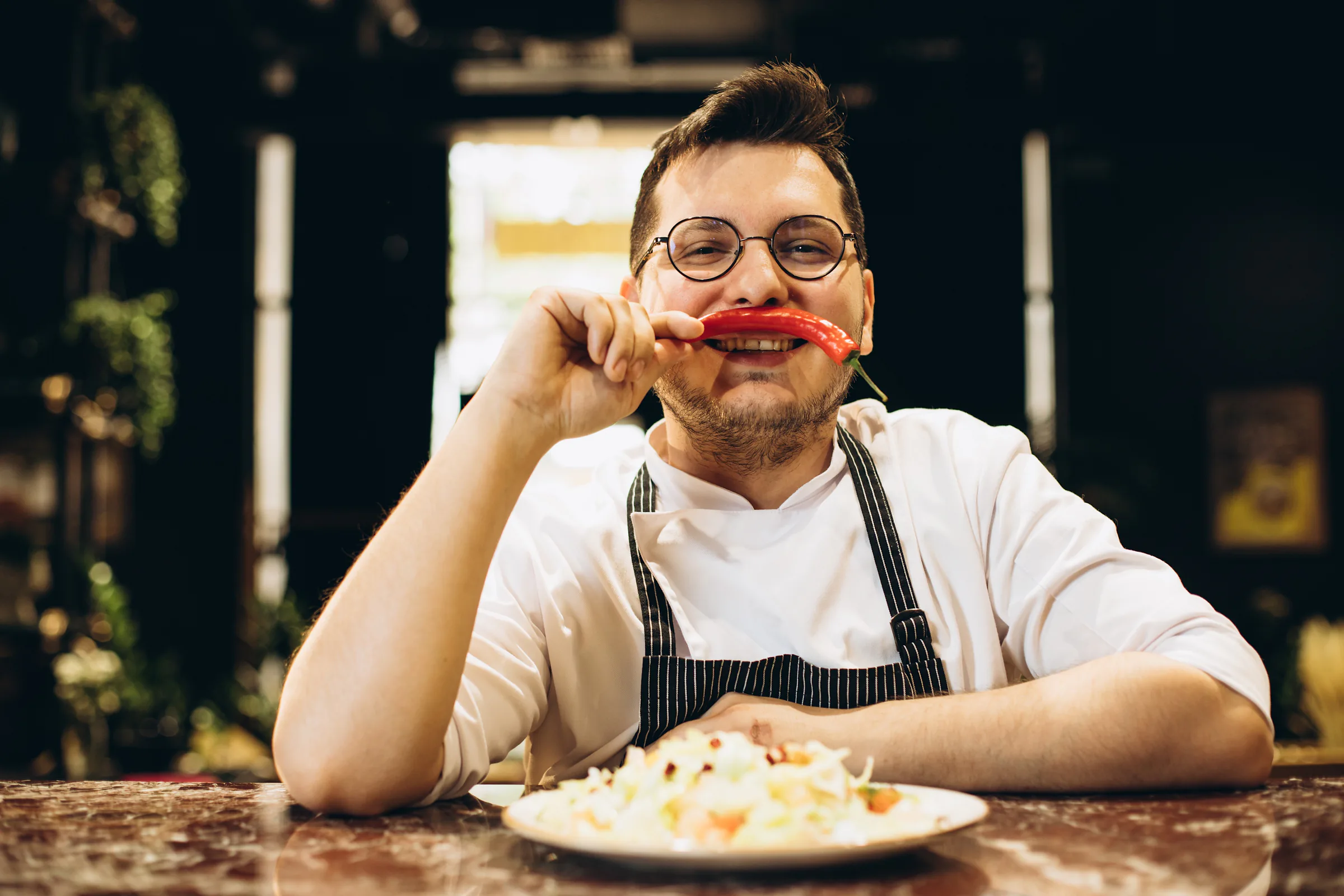 Chef sonriente sosteniendo un pimiento rojo en la cocina de un restaurante