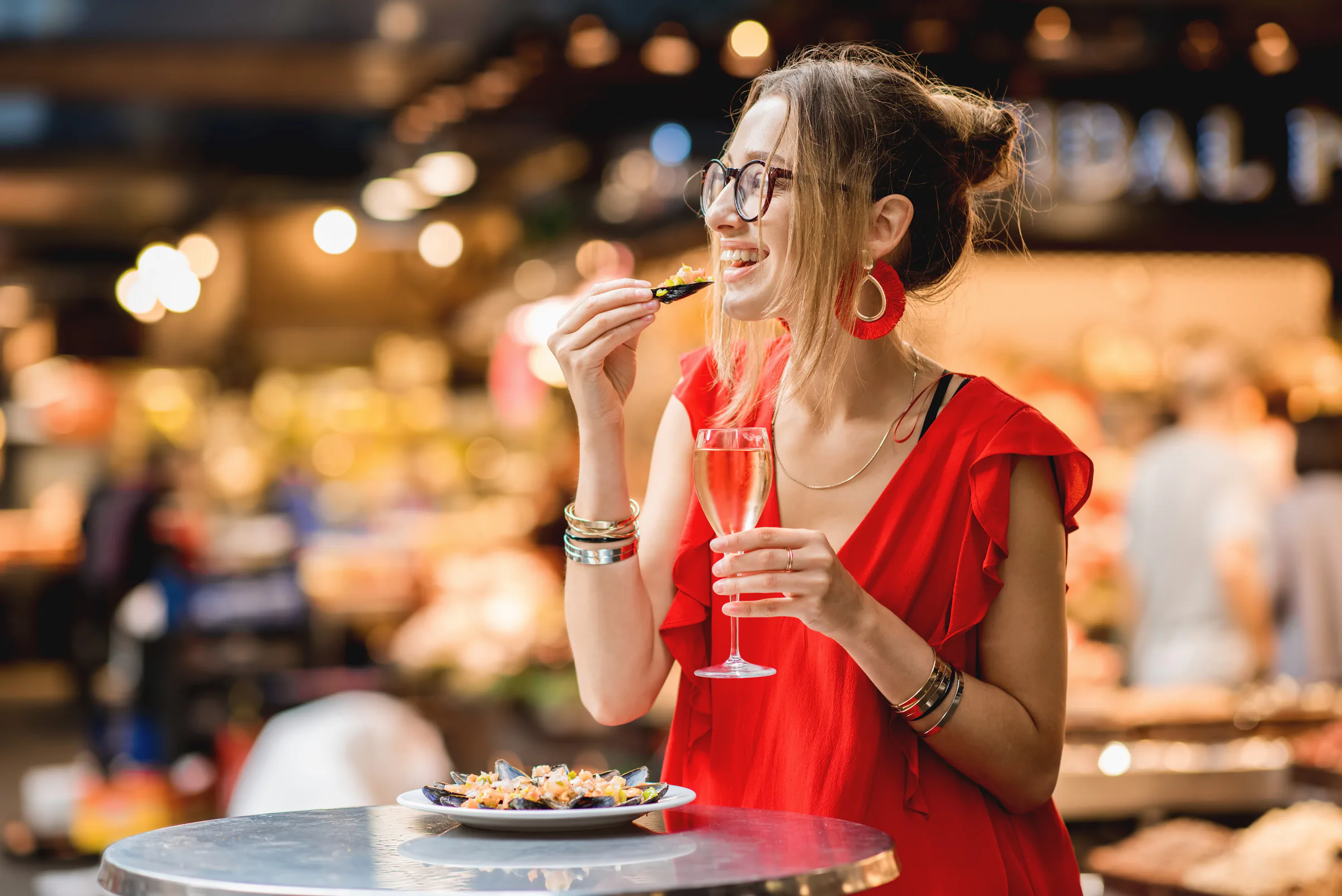 Clienta comiendo mejillones y tomando vino rosado en un mercado gastronómico