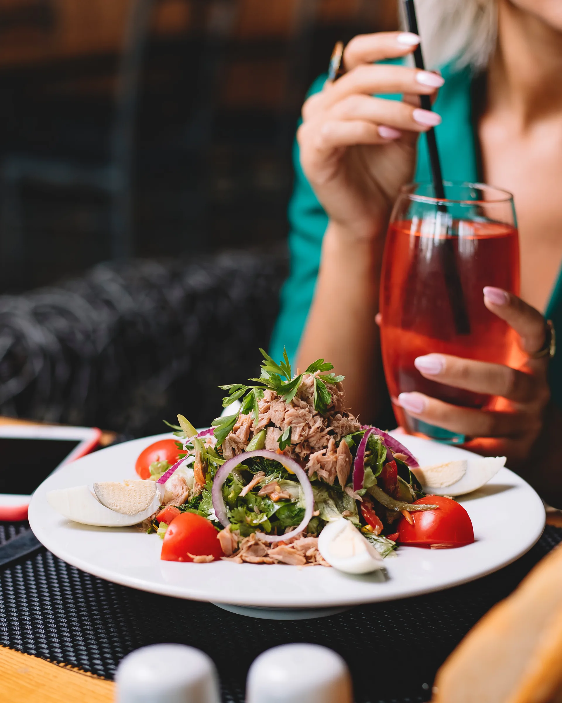 Ensalada de atún, huevo y tomate delante de una clienta con una bebida