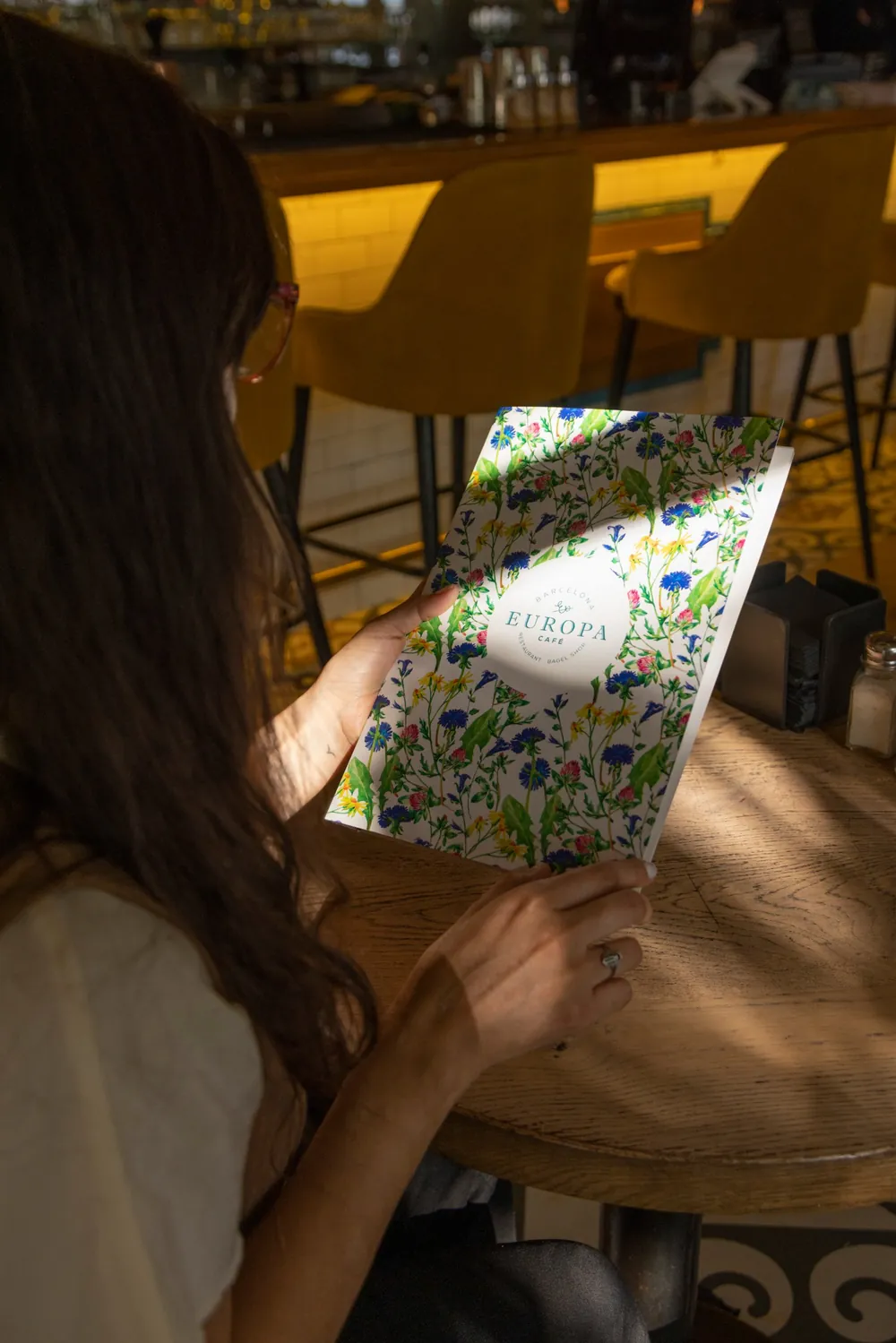 Clienta sujetando la carta de Europa Café, con portada ilustrada de flores silvestres